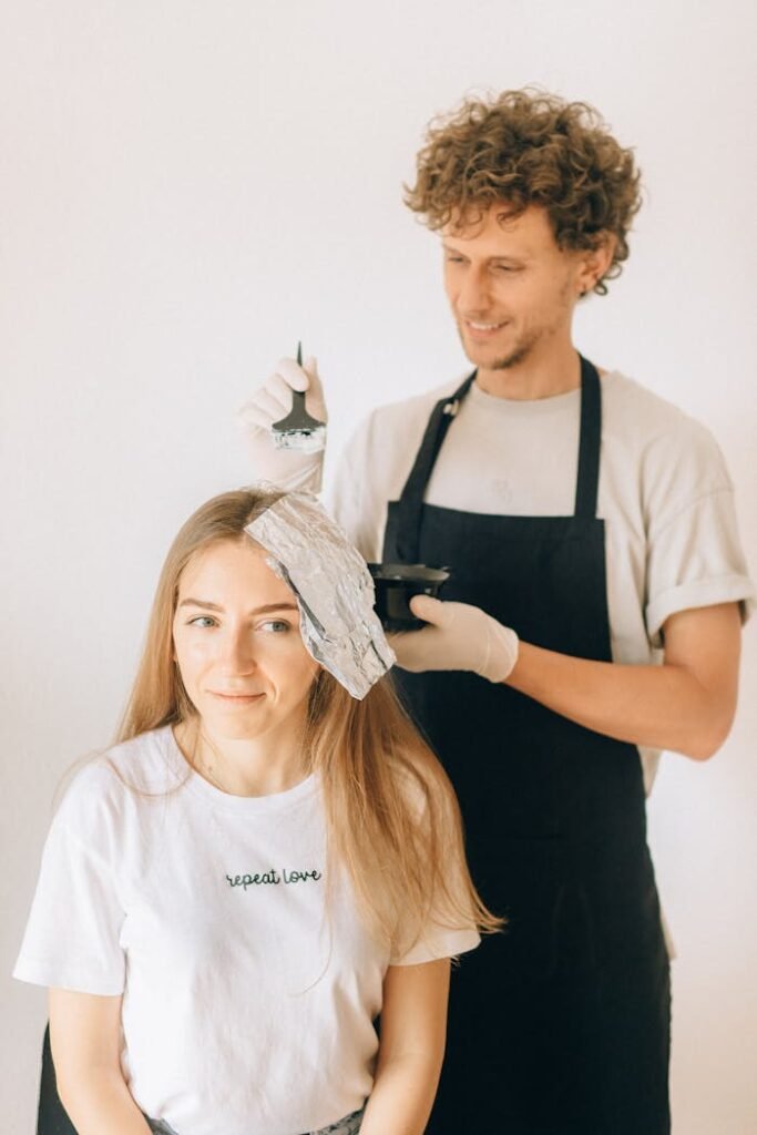 A Man in Black Apron Coloring a Woman's Hair